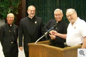 Grand Knight Dick Breckon presents a check to Bishop Taylor with Monsignor Friend and Father Elser observing.